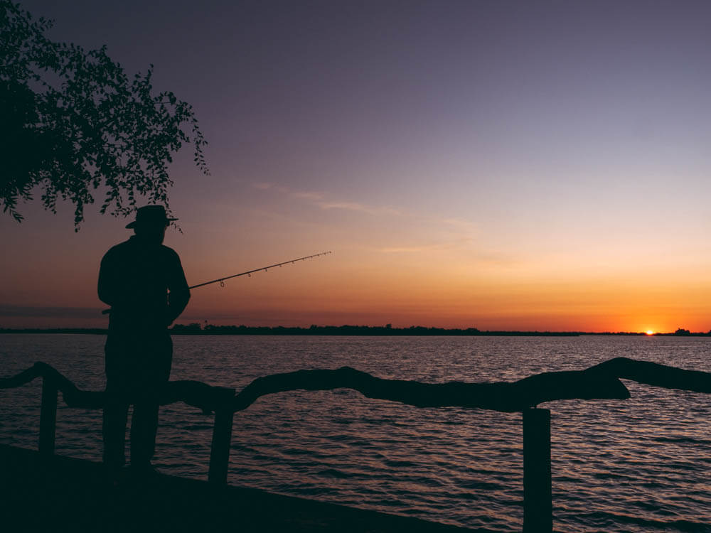 Silhouette of fisherman against sunset over body of water