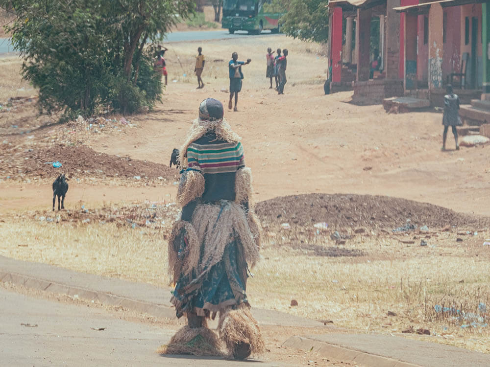 Gule Wamkulu dancer dressed in costume walking along the road