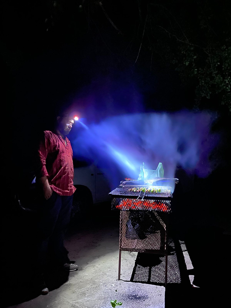John with headlamp looking at meat on fire